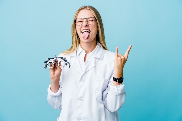 Giovane donna all'ottico optometrista russo su blu che mostra gesto di roccia con le dita