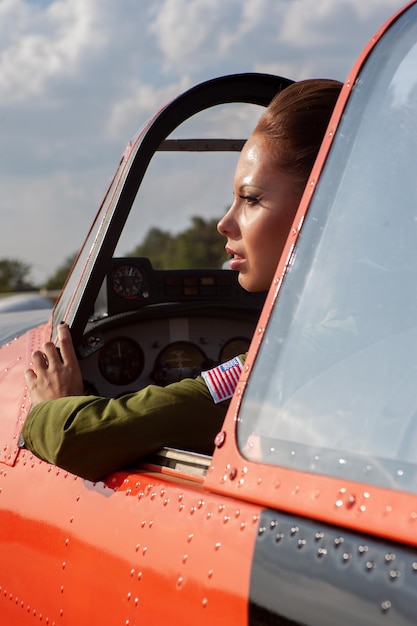 Giovane donna alla cabina di pilotaggio dell'aereo sullo sfondo delle nuvole.