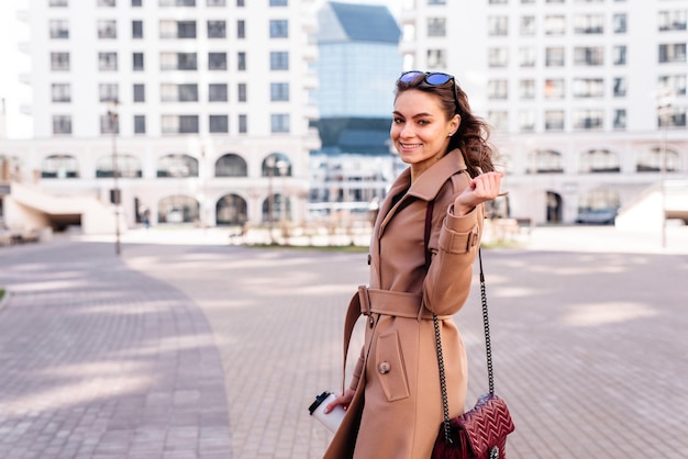 Giovane donna alla moda allegra che prende una tazza di caffè all'aperto che cammina