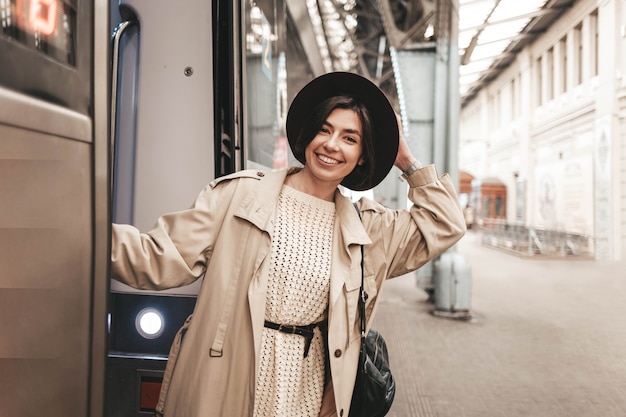 Giovane donna alla moda che appende e che sorride sul binario di un trasporto in treno.