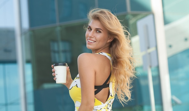 Giovane donna alla moda che beve caffè per andare in una strada cittadina