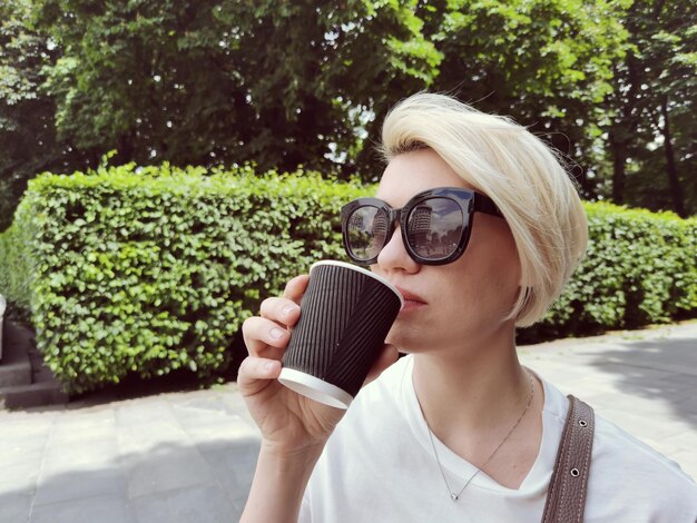 Giovane donna alla moda che beve caffè per andare in una strada cittadina.