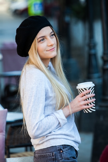 Giovane donna alla moda che beve il tè in una strada della città