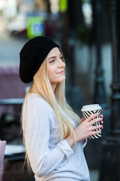 Giovane donna alla moda che beve il tè in una strada della città