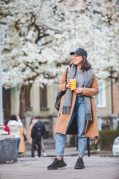 Giovane donna alla moda che cammina per strada con una tazza di caffè