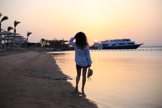 Giovane donna alla moda che posa vicino al lago il tramonto del giorno di estate