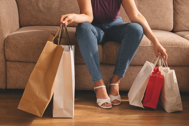 Giovane donna alla moda che tiene i sacchetti della spesa e che si siede su un divano