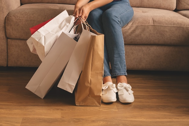 Giovane donna alla moda che tiene i sacchetti della spesa e che si siede su un divano