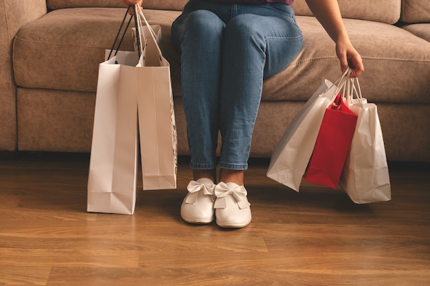 Giovane donna alla moda che tiene i sacchetti della spesa e che si siede su un divano