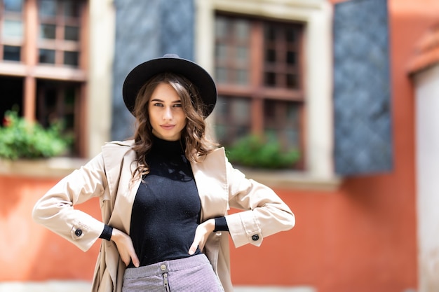 Giovane donna alla moda in cappello e cappotto in posa in strada.