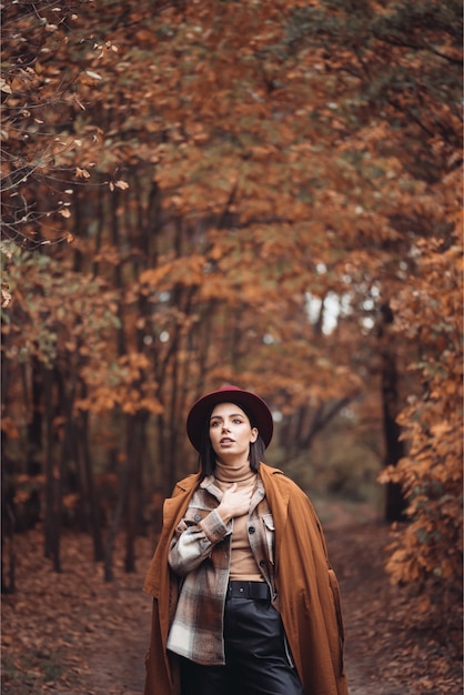 Giovane donna alla moda in una foresta secca di autunno