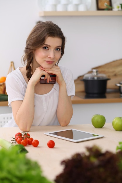 Giovane donna alla ricerca di una nuova ricetta per cucinare in cucina. La casalinga sta facendo acquisti online tramite tablet e carta di credito.