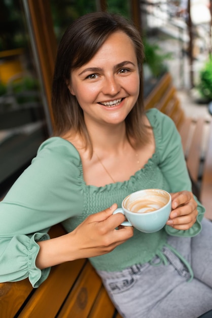 Giovane donna allegra che beve caffè al caffè all'aperto Donna piacevole che beve caffè