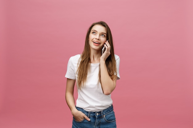 Giovane donna allegra che parla sul telefono cellulare isolato su fondo rosa