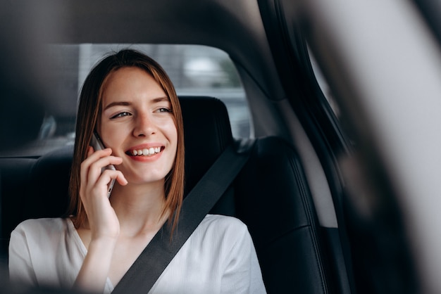 Giovane donna allegra che parla uno smartphone che si siede nell'automobile.