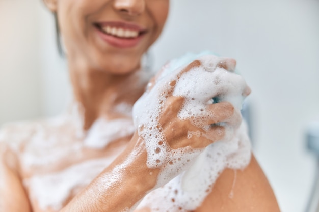 Giovane donna allegra che si lava il corpo con la luffa da bagno