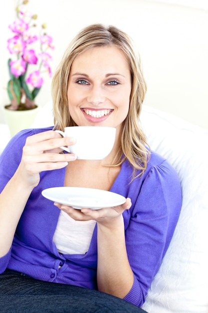 Giovane donna allegra che tiene una tazza di caffè su un sofà