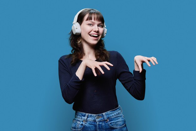 Giovane donna allegra con le cuffie che balla una danza alla moda sullo sfondo blu