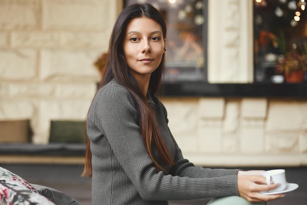 Giovane donna allegra con una tazza di caffè che si siede al caffè che sorride all'aperto