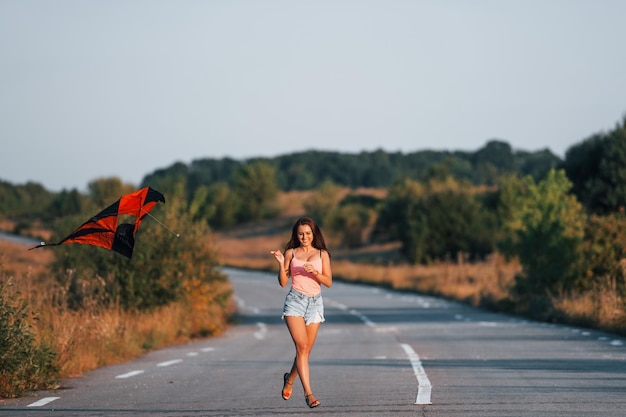 Giovane donna allegra divertendosi con l'aquilone all'aperto sulla strada