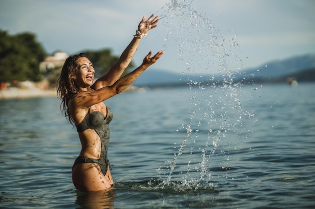 Giovane donna allegra divertendosi sulla spiaggia. Sta sguazzando nell'acqua di mare e si diverte in vacanza.