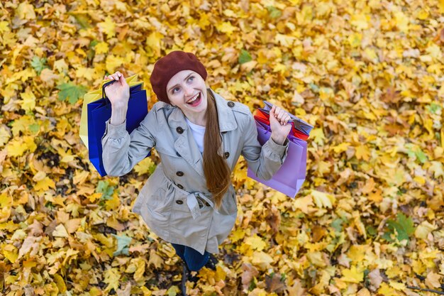 Giovane donna allegra felice con gli acquisti nelle mani che camminano nella sosta di autunno