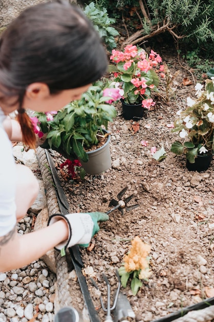 Giovane donna allegra in guanti che utilizza attrezzi da giardinaggio per piantare fiori sul cortile posteriore casual