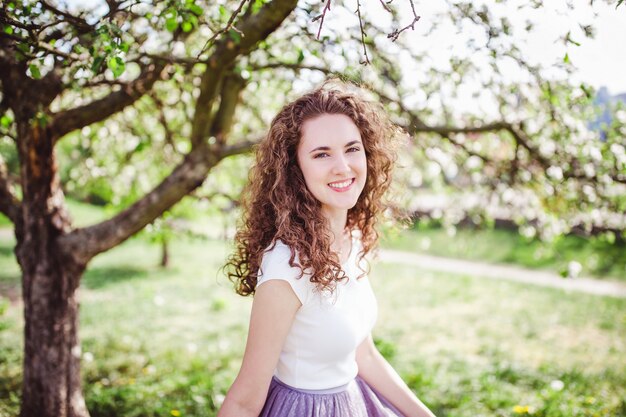 Giovane donna allegra in una maglietta bianca sotto l'albero di fioritura.