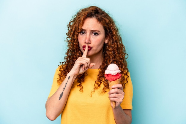 Giovane donna allo zenzero che tiene un gelato isolato su sfondo blu mantenendo un segreto o chiedendo silenzio