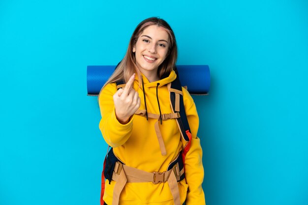 Giovane donna alpinista con un grande zaino isolato sull'azzurro che fa gesto venente