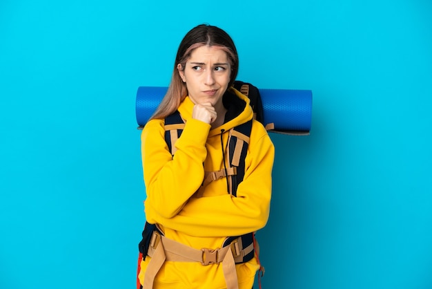 Giovane donna alpinista con un grande zaino isolato sull'azzurro che ha dubbi e pensiero