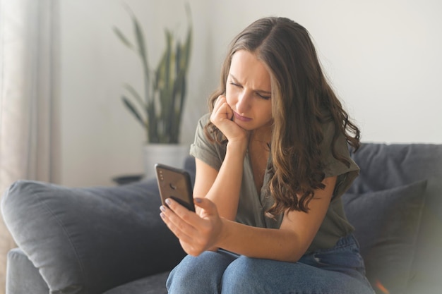 Giovane donna annoiata con lo smartphone seduta sul divano