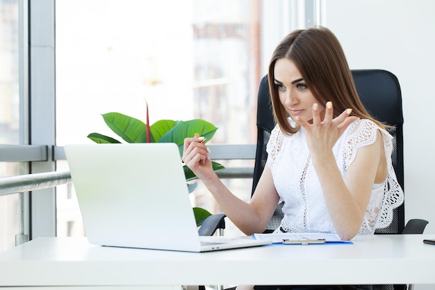 Giovane donna annoiata nell&#39;ufficio che lavora con un computer portatile e che fissa allo schermo di computer