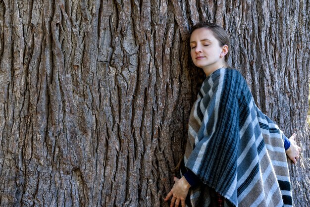 Giovane donna appoggiata al tronco di un grande albero. Occhi chiusi. Unità con la natura