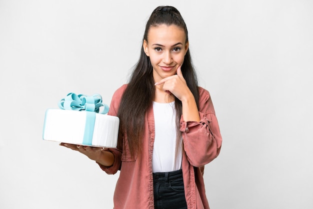 Giovane donna araba che tiene la torta di compleanno su sfondo bianco isolato pensando