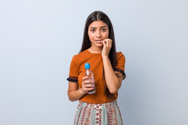 Giovane donna araba che tiene le unghie mordaci di una bottiglia di acqua, nervose e molto ansiose.