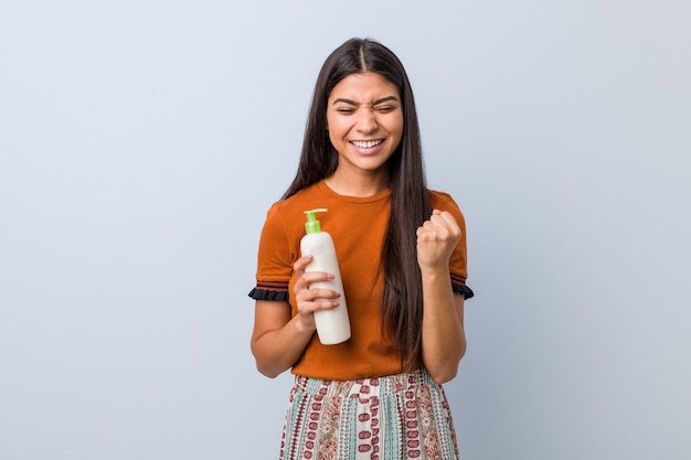 Giovane donna araba che tiene una bottiglia crema incoraggiante spensierata ed eccitata. Concetto di vittoria.