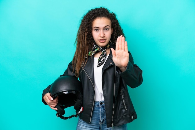 Giovane donna araba con un casco da motociclista isolato su sfondo blu che fa un gesto di arresto