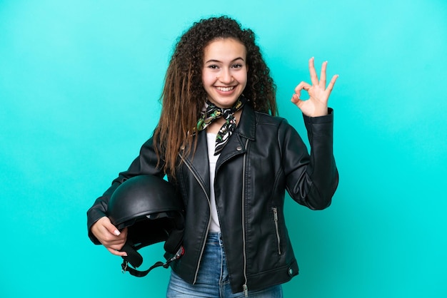 Giovane donna araba con un casco da motociclista isolato su sfondo blu che mostra il segno ok con le dita