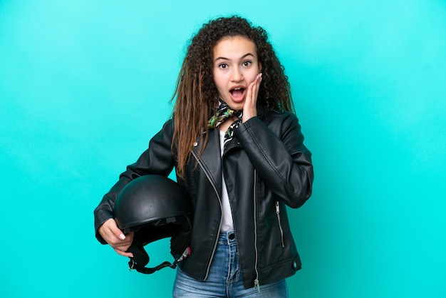 Giovane donna araba con un casco da motociclista isolato su sfondo blu con espressione facciale sorpresa e scioccata