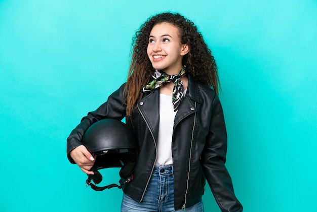 Giovane donna araba con un casco da motociclista isolato su sfondo blu pensando a un'idea mentre guarda in alto
