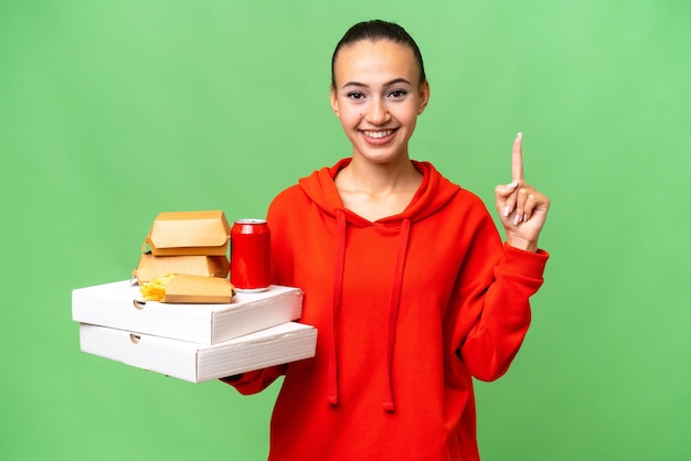 Giovane donna araba holding fast food su sfondo isolato che punta verso l'alto una grande idea