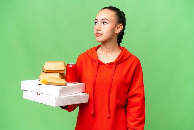 Giovane donna araba holding fast food su sfondo isolato guardando al lato