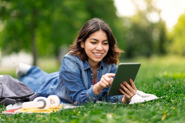 Giovane donna araba sorridente che naviga sui social media sulla tavoletta digitale all'aperto