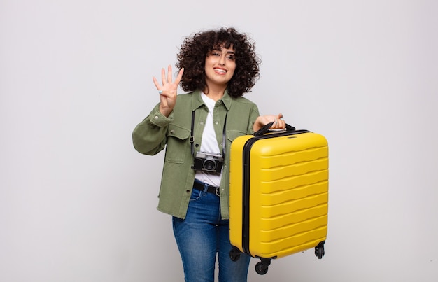 Giovane donna araba sorridente e guardando amichevole, mostrando il numero quattro o quarto con la mano in avanti, contando il concetto di viaggio