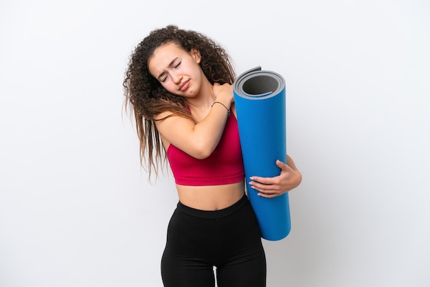 Giovane donna araba sportiva che va a lezioni di yoga mentre tiene un tappetino isolato su sfondo bianco che soffre di dolore alla spalla per aver fatto uno sforzo