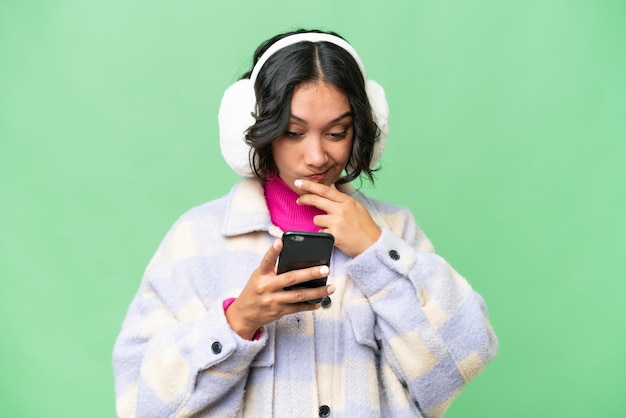 Giovane donna argentina che indossa muffi invernali su uno sfondo isolato che pensa e manda un messaggio