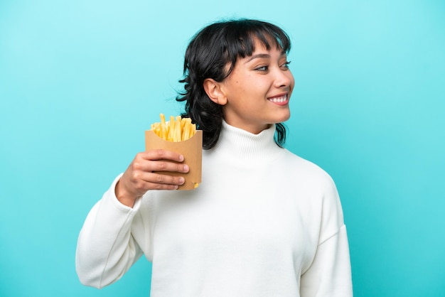 Giovane donna argentina che tiene patatine fritte isolate su sfondo blu guardando lato