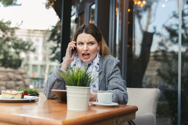 Giovane donna arrabbiata che risolve i problemi di affari che grida durante la conversazione telefonica