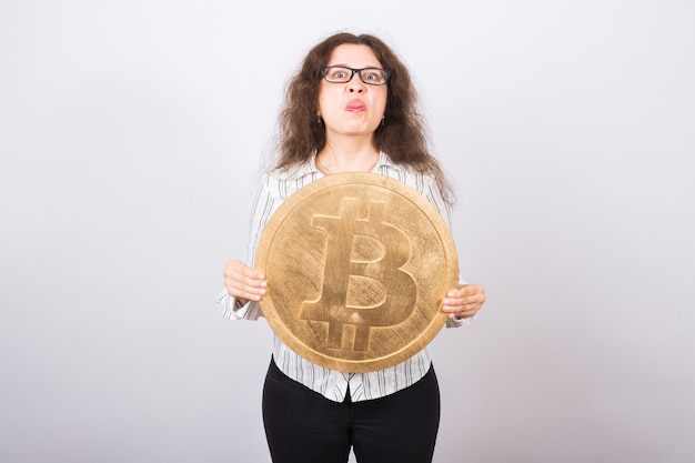 Giovane donna arrabbiata che tiene grande bitcoin dorato e che mostra la lingua - valuta crittografica, denaro web e